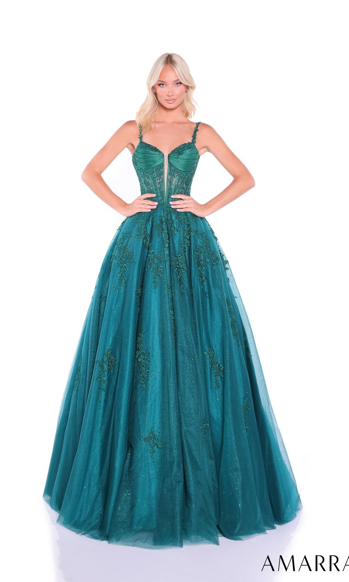 A woman stands with her hands on her hips against a white background, wearing the Amarra 89493 Lace-Up Long Corset Prom Ball Gown in emerald, featuring a sleeveless fitted bodice and floral embroidery.